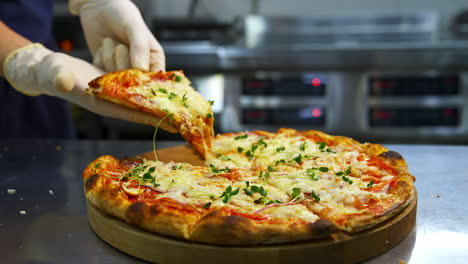 delicious pizza on wooden board. hands in gloves taking one piece of ready pizza. well-baked pizza with melted cheese in the restaurant.