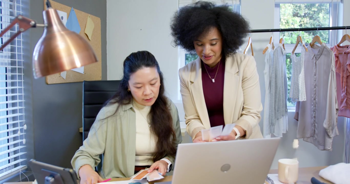 Team di donne diverse che si scambiano campioni, segnando i campioni con una penna rosa e controllando il laptop per il design