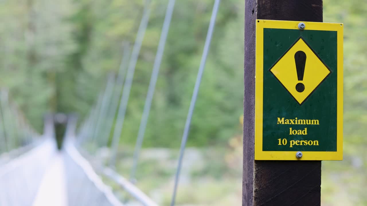 Camera moves toward warning sign on forest suspension bridge, natural daylight, shallow depth of field