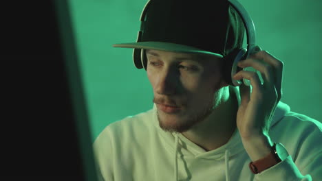 portrait of a modern man with cap and wireless headphones on a neon light colorful background. close-up.