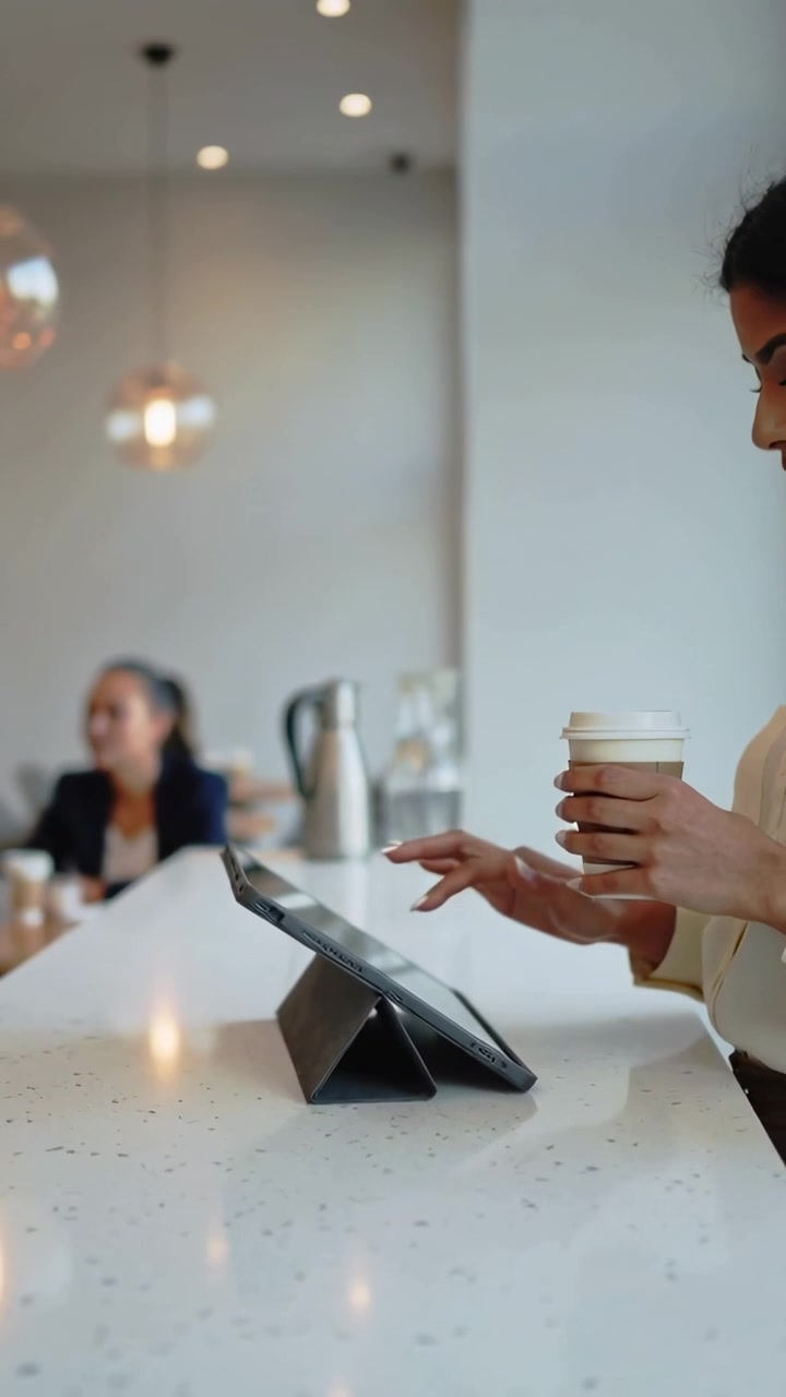 Video verticale: Bancone del bar in movimento, donna in camicetta che tiene una tazza e usa un tablet con custodia, spazio per il testo