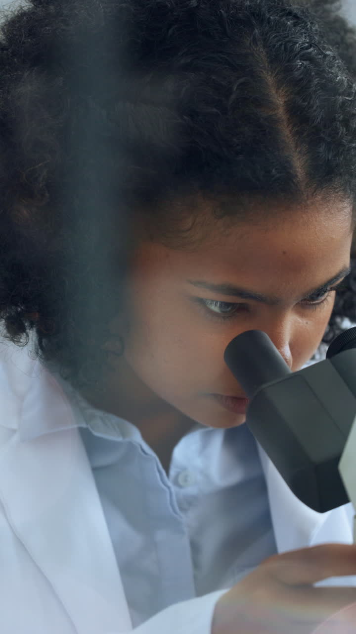 Giovane scienziata che guarda attraverso il microscopio in laboratorio