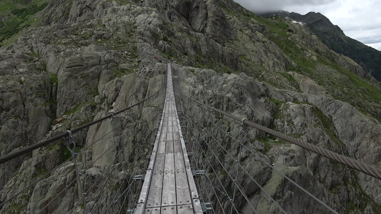 Point of view shot moving forward along Trift Bridge, a narrow suspension footbridge above a rocky alpine gorge near Gadmen, Bernese Oberland, Switzerland