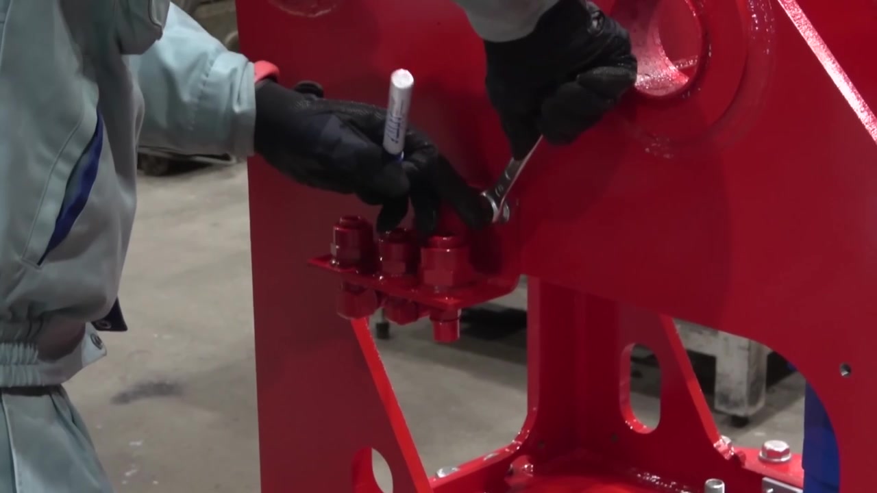 Operaio addetto all'assemblaggio che stringe bulloni grandi con una chiave inglese su un telaio in acciaio rosso appena verniciato di macchinari edili