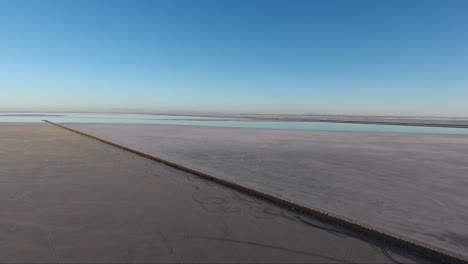 a drone shot flying over the bonneville salt flats shows the salt flats causeway and distant highway