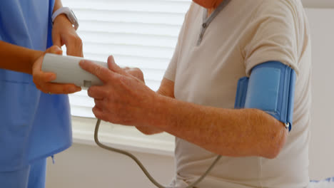 Side-view-of-young-Caucasian-female-doctor-showing-blood-pressure-reading-to-senior-man-at-home-4k