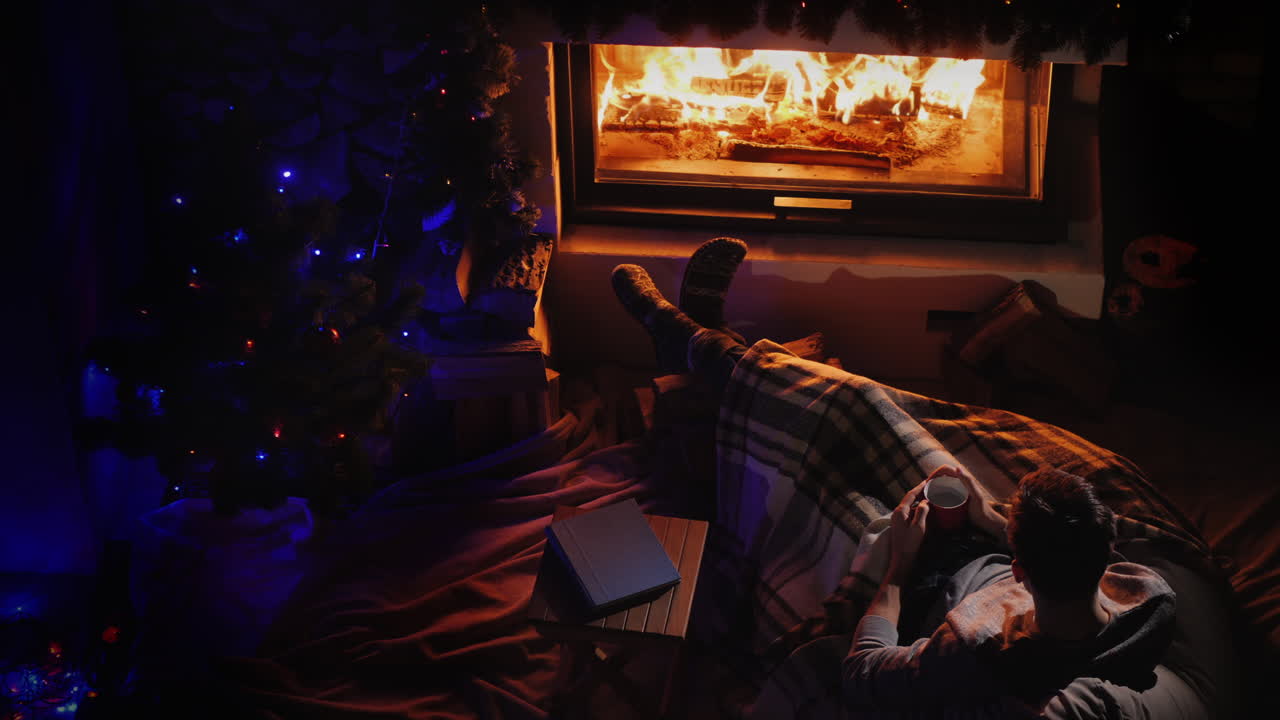 벽난로 옆의 멋진 저녁과 새해 나무 한 남자가 벽난로의 불을 존경합니다