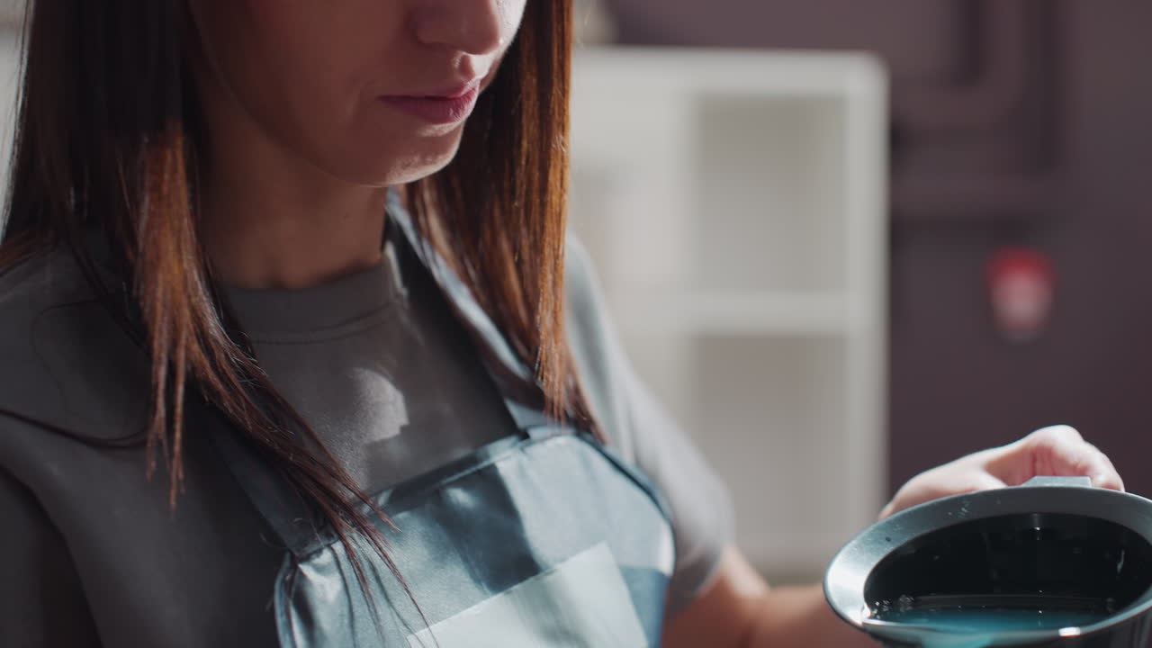 파란색 염색약을 그릇에 붓고 있는 흰색 스타일리스트, 집중한 표정, 현대적인 살롱 인테리어, 액체 측정, 조심스러운 손길, 검은색 혼합 그릇, 흐릿한 병 라벨, 부드러운 자연광, 차분한 색조