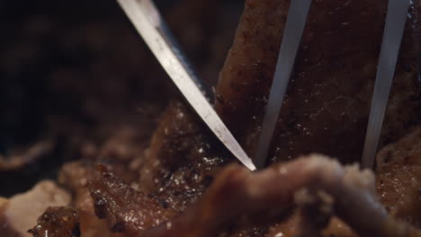 fork holds juicy meat in place for scissors to cut portion, close-up