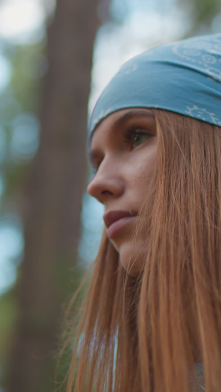 una mujer caminando a través de un bosque vibrante, mirando hacia abajo contemplativamente, con un pañuelo azul y una mochila, rodeada de árboles altos y vegetación exuberante con luz cálida filtrándose a través de las hojas