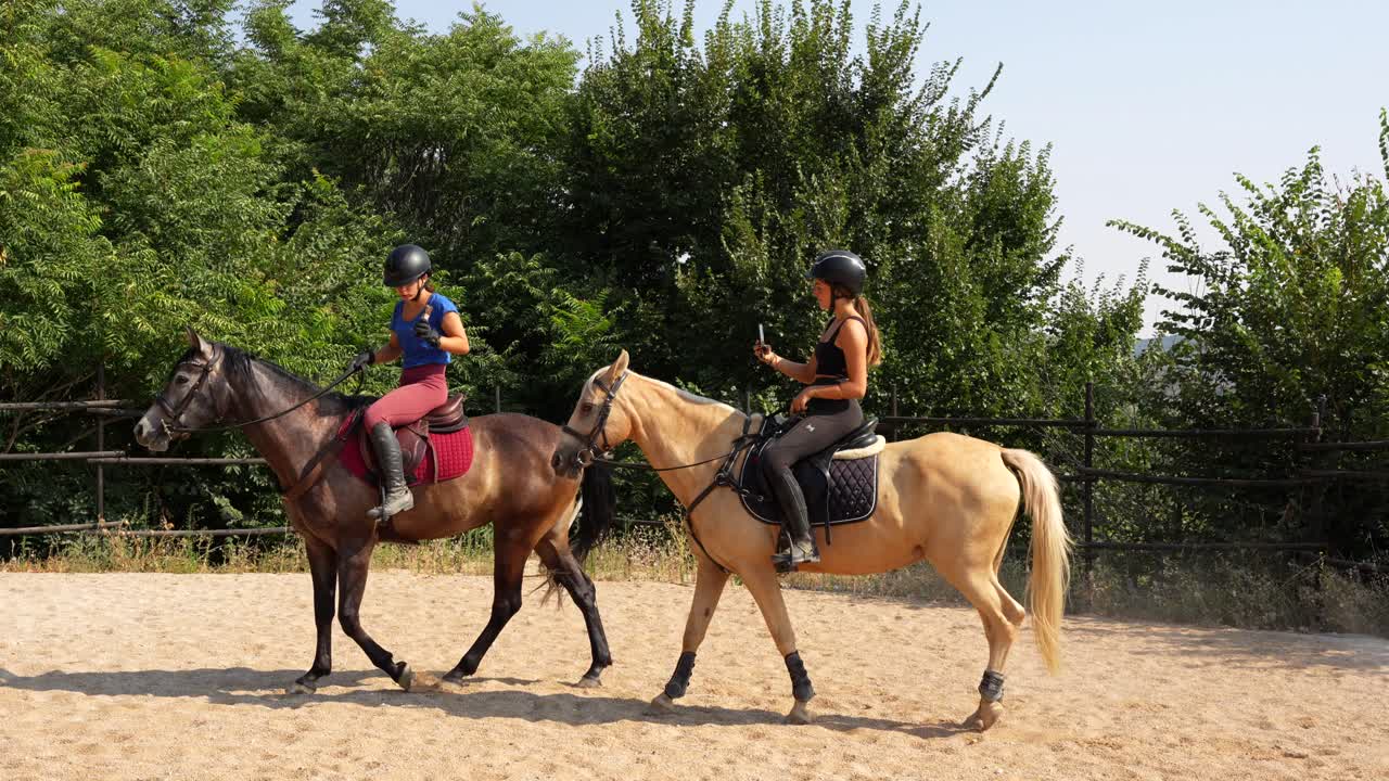 Two women record each other while riding in the arena as part of a training session