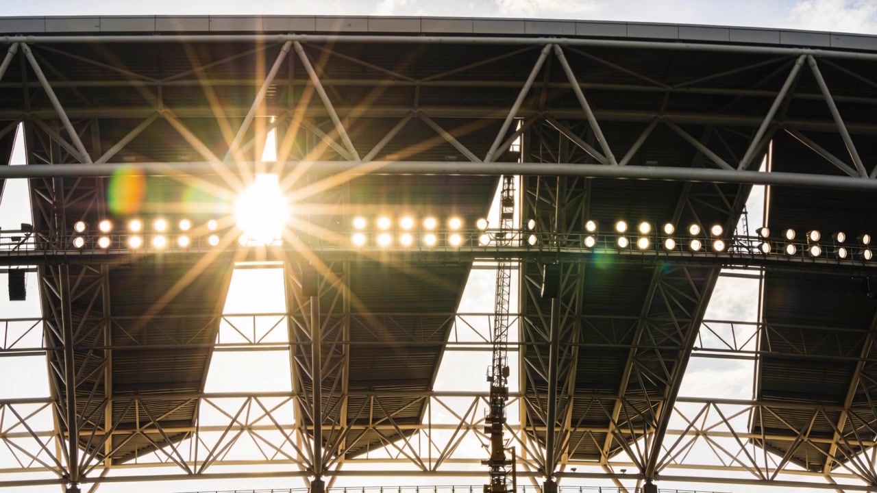 Shining sun passing through roof gap at stadium shifting lens flare across trusses and lights