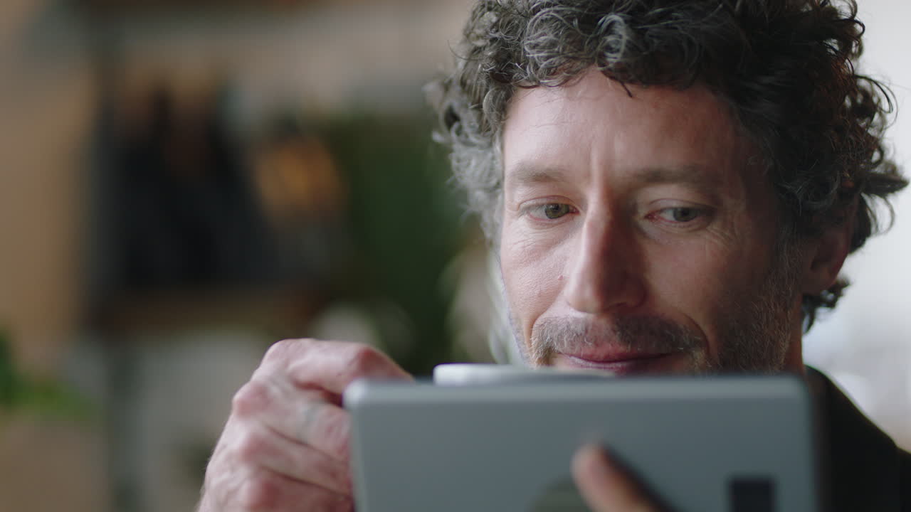 atractivo hombre de negocios caucásico en un café usando una tableta viendo entretenimiento en línea leyendo mensajes de redes sociales disfrutando bebiendo café relajándose