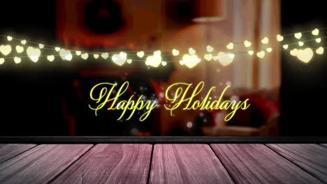 Happy-holidays-text-and-glowing-yellow-heart-shaped-fairy-light-decoration-over-wooden-plank