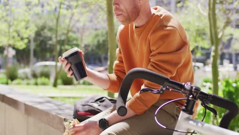 Albino-african-american-man-with-dreadlocks-sitting-in-park-with-bike-drinking-coffee