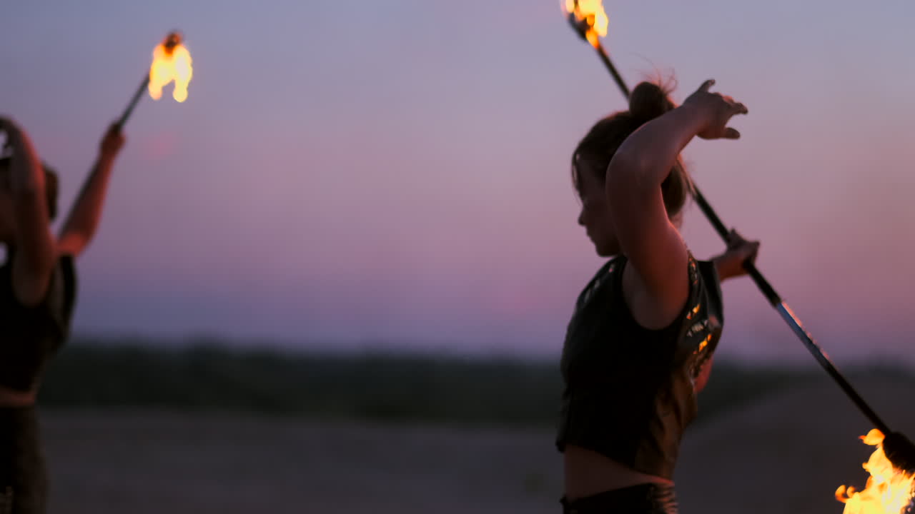 Women with fire at sunset on the sand dance and show tricks against the beautiful sky in slow motion