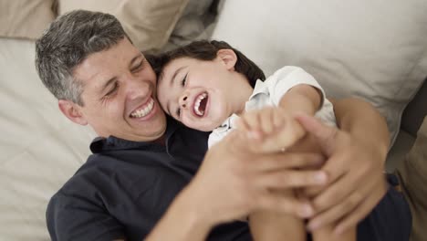 padre alegre acurrucando y cosquilleando sonriendo hijo pequeño
