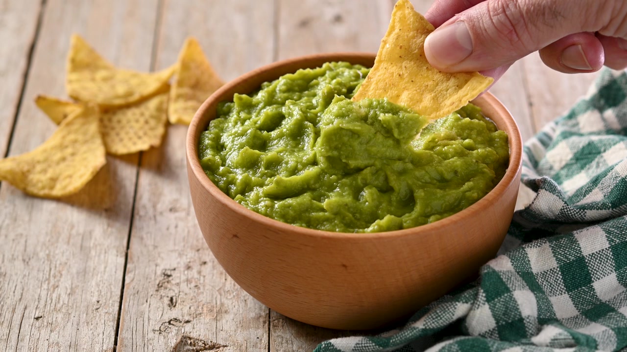 Člověk namáčí guacamole s nacho lupínkem