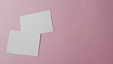 Overhead-view-of-two-blank-white-business-cards-on-pink-background,-copy-space,-slow-motion