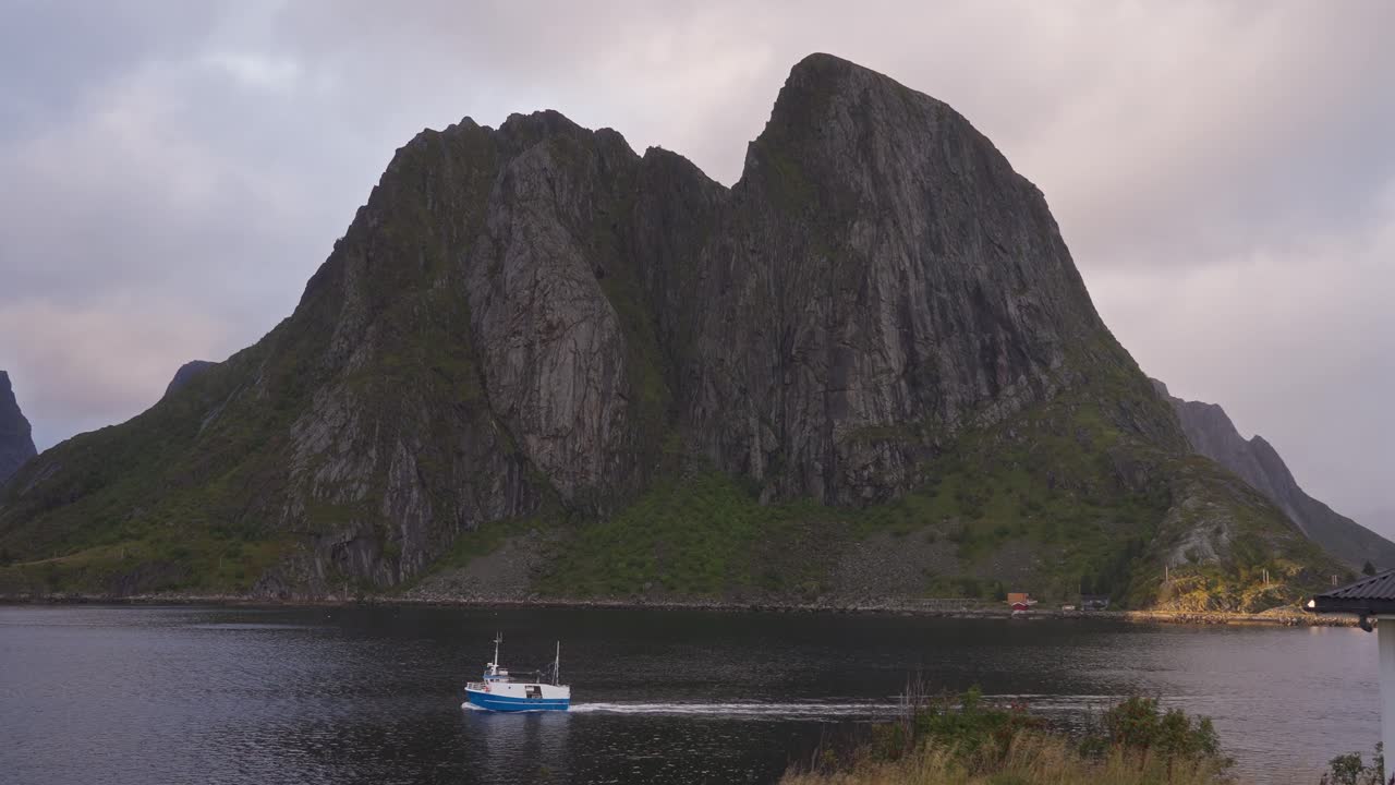 movimiento lento de un barco de pescador que pasa por delante de las montañas de hamnøy cerca de reine, islas lofoten, noruega
