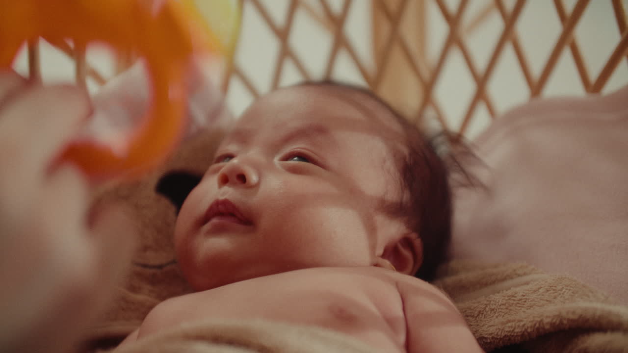 Peaceful newborn infant baby enjoying playing with parents hand while holding a kids toy laying in wooden cradle soft warm light