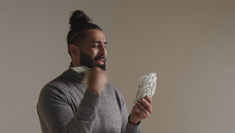 studio shot of excited man celebrating winning cash prize throwing handful of 100 dollar bills in the air