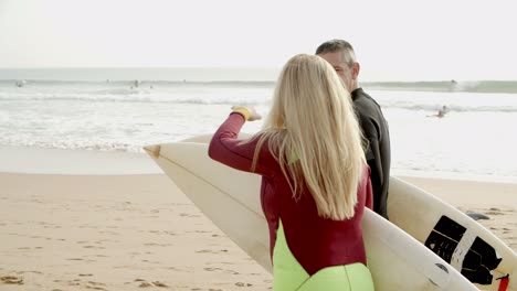 couple with surfboards walking on beach