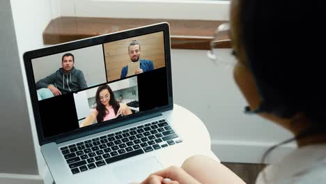 young woman working at home during quarantine. girl with headphones look at laptop screen. video call with two men and one woman. online conversation and conference. team meeting. side back view.