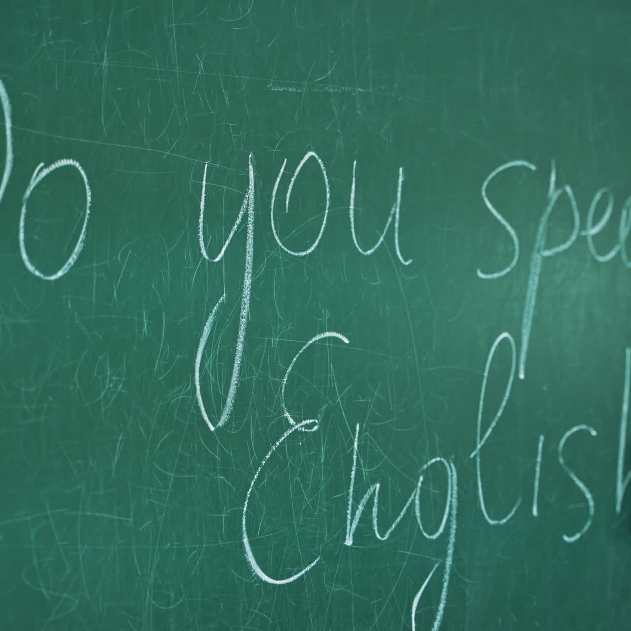 Female's hand is wiping from the blackboard. Teacher wipes the English inscription with sponge on the green board background.