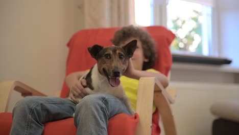 blond boy sitting on the chair while swinging with his dog and caresses him