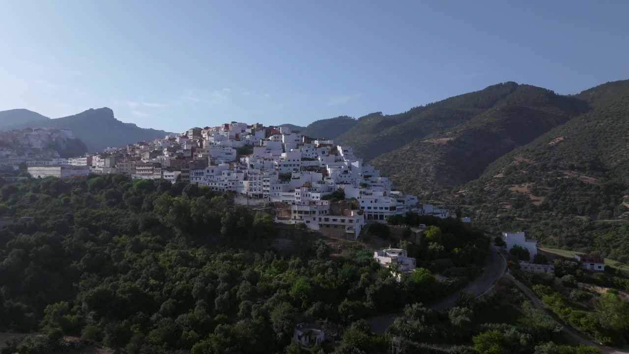 Vista aerea con drone di Moulay Idriss Zerhoun, la storica città bianca collinare del Marocco settentrionale, che si erge sopra una fitta vegetazione e incorniciata dalle pittoresche montagne di Zerhoun