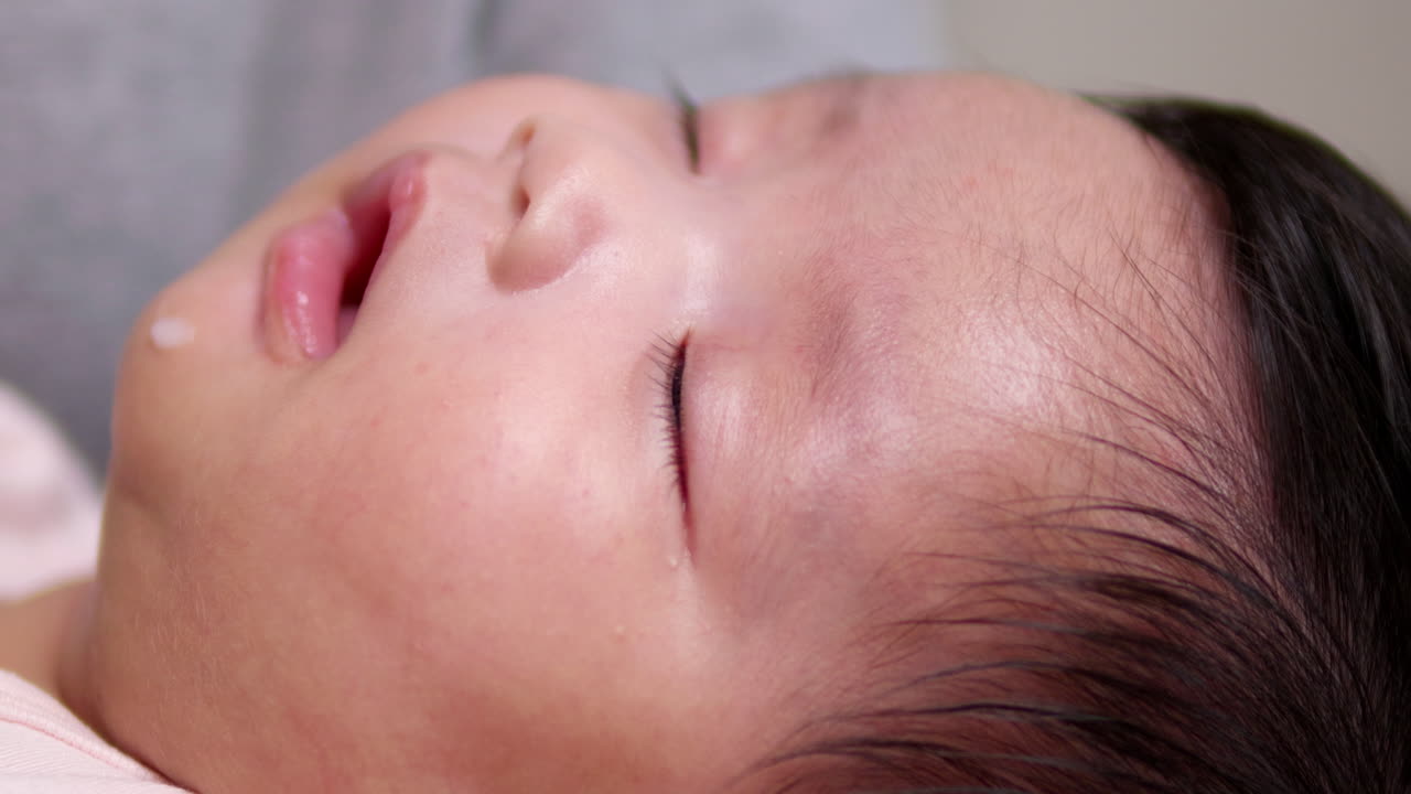 Adorable sleepy baby drowsily falling asleep after feeding with a milk droplet on the mouth. A tender peaceful moment captured