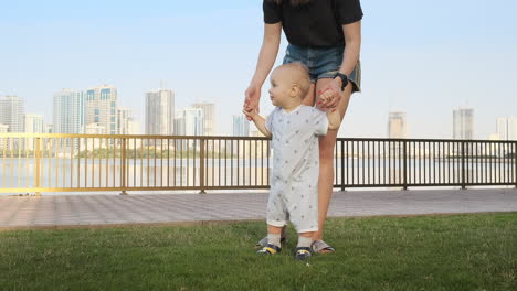 un niño sonriente sosteniendo la mano de su madre hace los primeros pasos caminando por el paseo marítimo en verano.