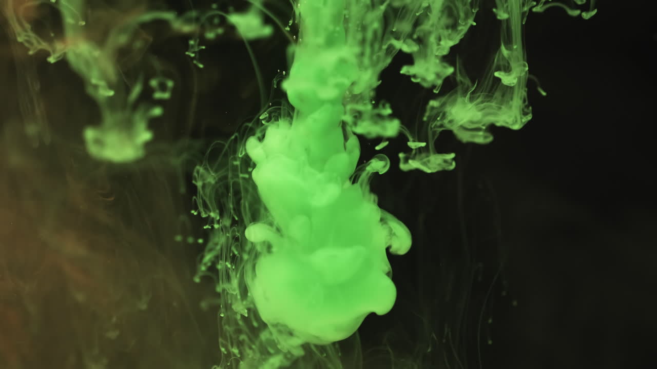 Slow motion video of green watercolor ink mixing in water against black background