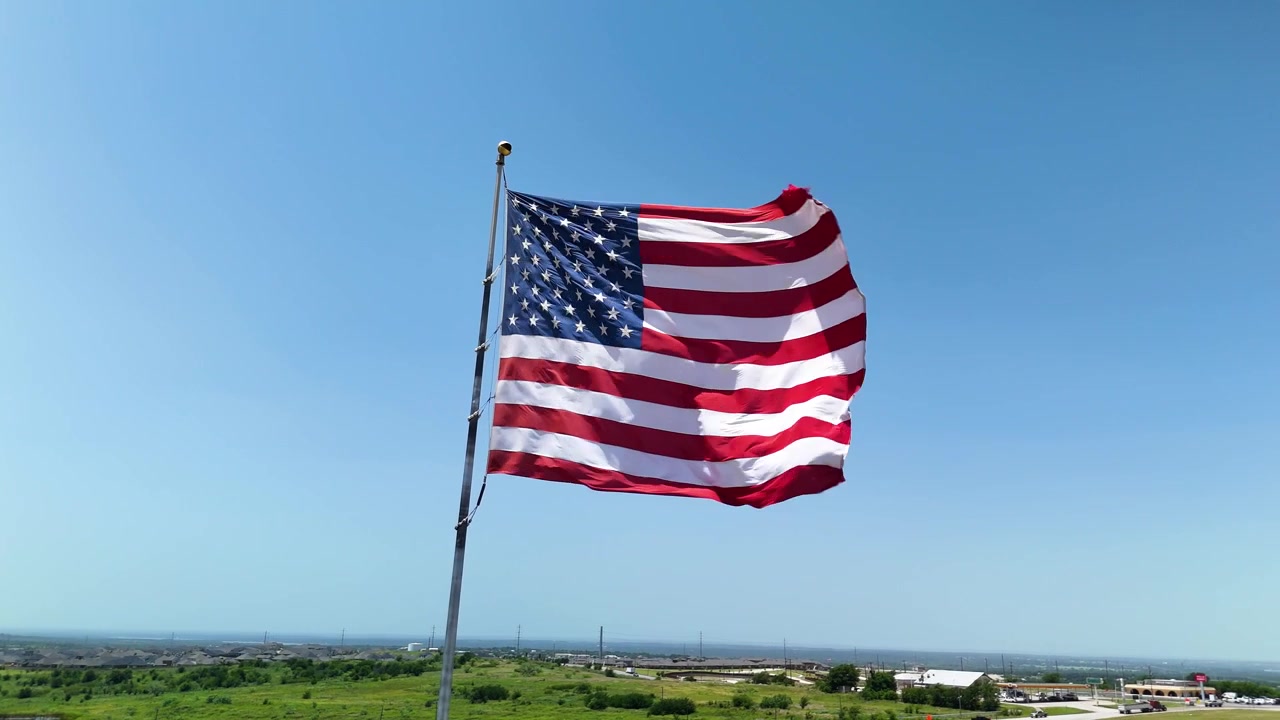 Filmisk stockoptagelse af det amerikanske flag, der vajer stolt i den stærke vind under skarpt sollys. B-roll af høj kvalitet til patriotiske og kommercielle projekter.