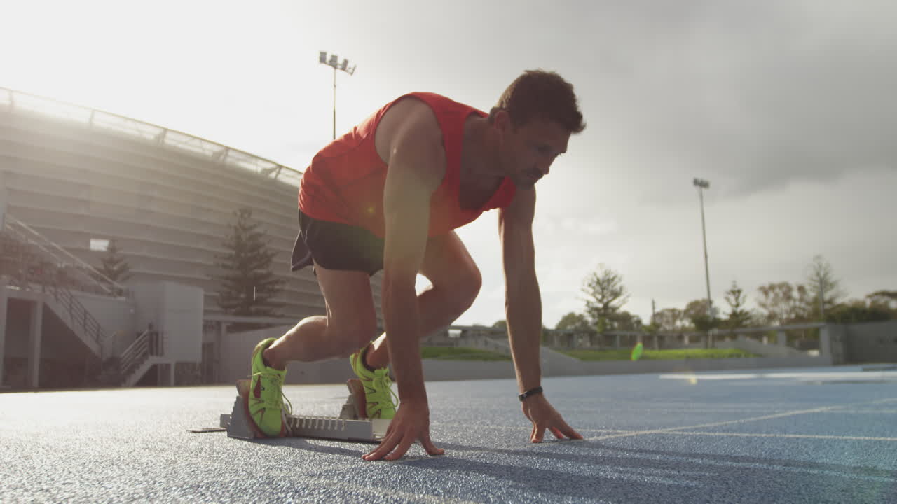 vista lateral de un atleta caucásico preparándose para una carrera en un estadio