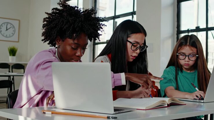 High-angle video of diverse students collaborating at a table with laptops and books, in a bright