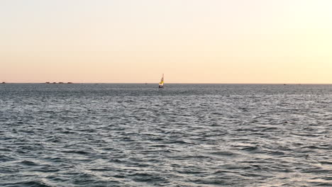 Toma-Aérea-Baja-De-Un-Pequeño-Velero-Al-Atardecer-Navegando-A-Lo-Largo-Del-Horizonte-Del-Océano