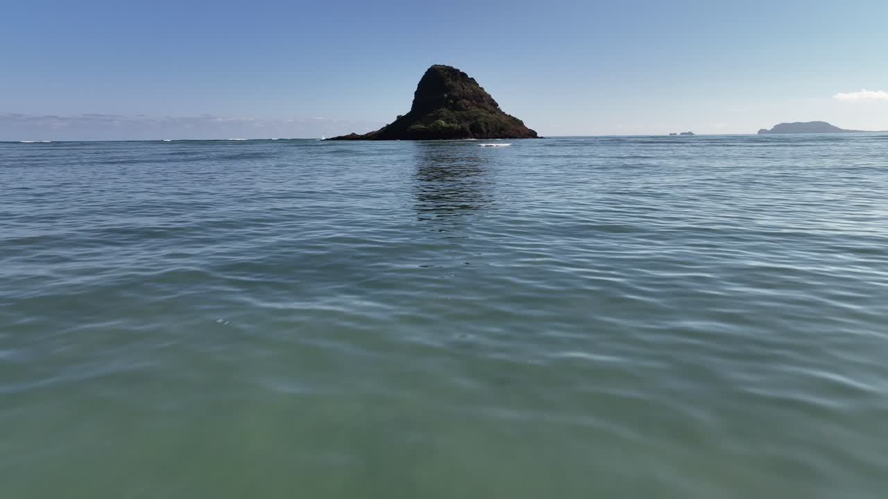 오아후섬의 카네오헤 베이 하와이에 있는 차이나맨 모자의 60fps 느린 모 드론 공중 영상이 섬 위로 패닝하고 푸른 바다를 한낮의 햇살을 보여줍니다.