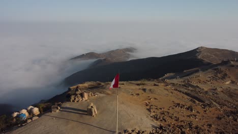 peruvian flag planted on top a mountain, above a layer of clouds