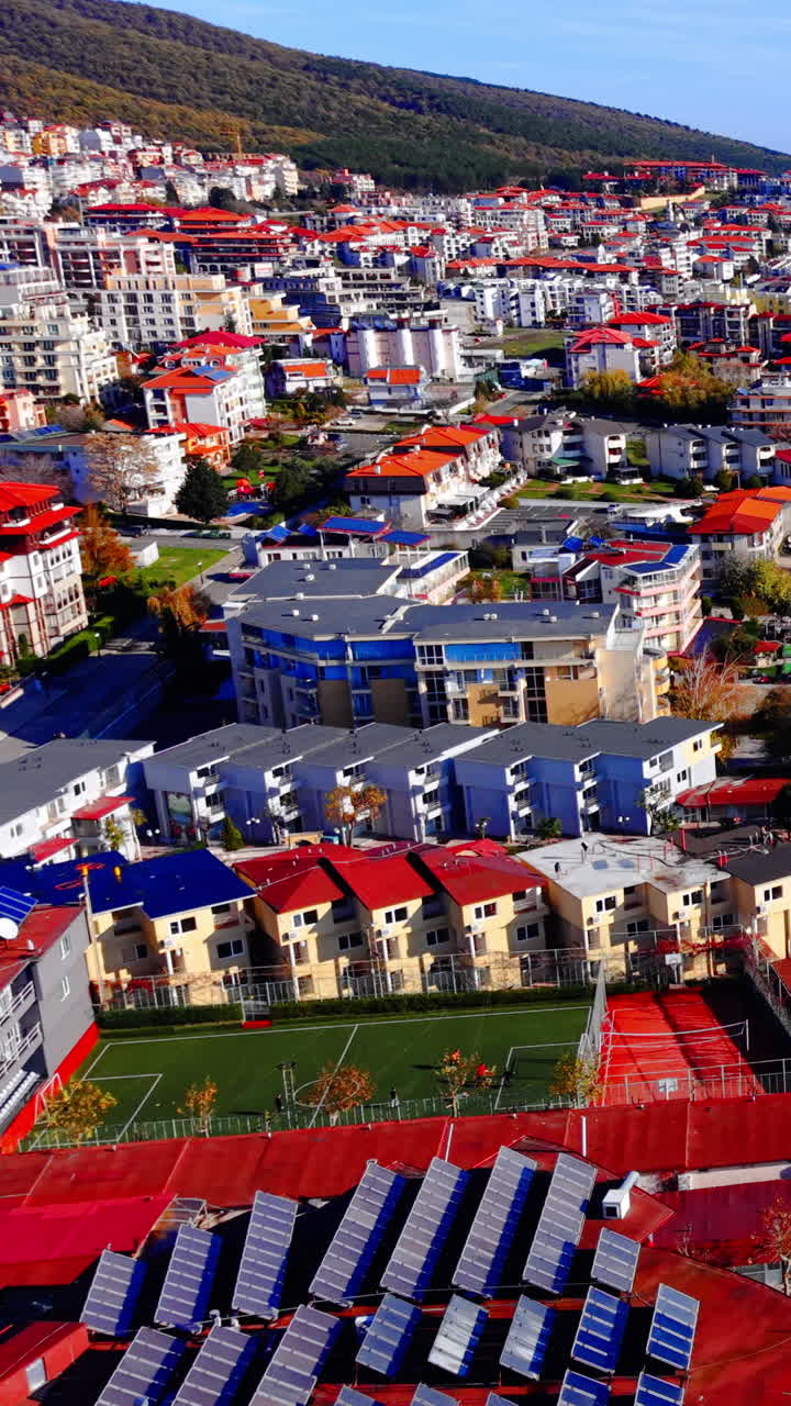 Beyaz ve gri binaların düz çatılarında çok sayıda güneş paneli kurulumu bulunan bir yerleşim bölgesi. Modern şehir tatil köyü binalarının çatıları. Dikey video