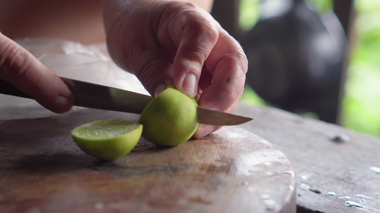 anciana usando un cuchillo para cortar limón verde por encima de la tabla de madera. agua dentro salpicando.
