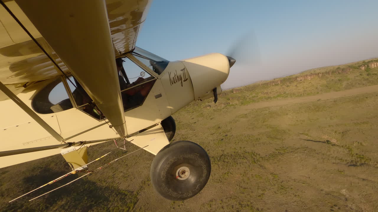Avião sobre a savana com vista aérea de uma falésia rochosa distante.