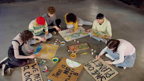 top view of young environmental activists painting placards sitting on the floor