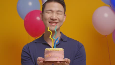 studio portrait of man wearing party hat celebrating birthday blowing out candles on cake 1