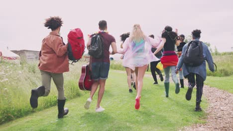 grupo de jóvenes amigos corriendo a través de barreras en la entrada del sitio del festival de música y hacia el escenario visto desde atrás - filmado en cámara lenta