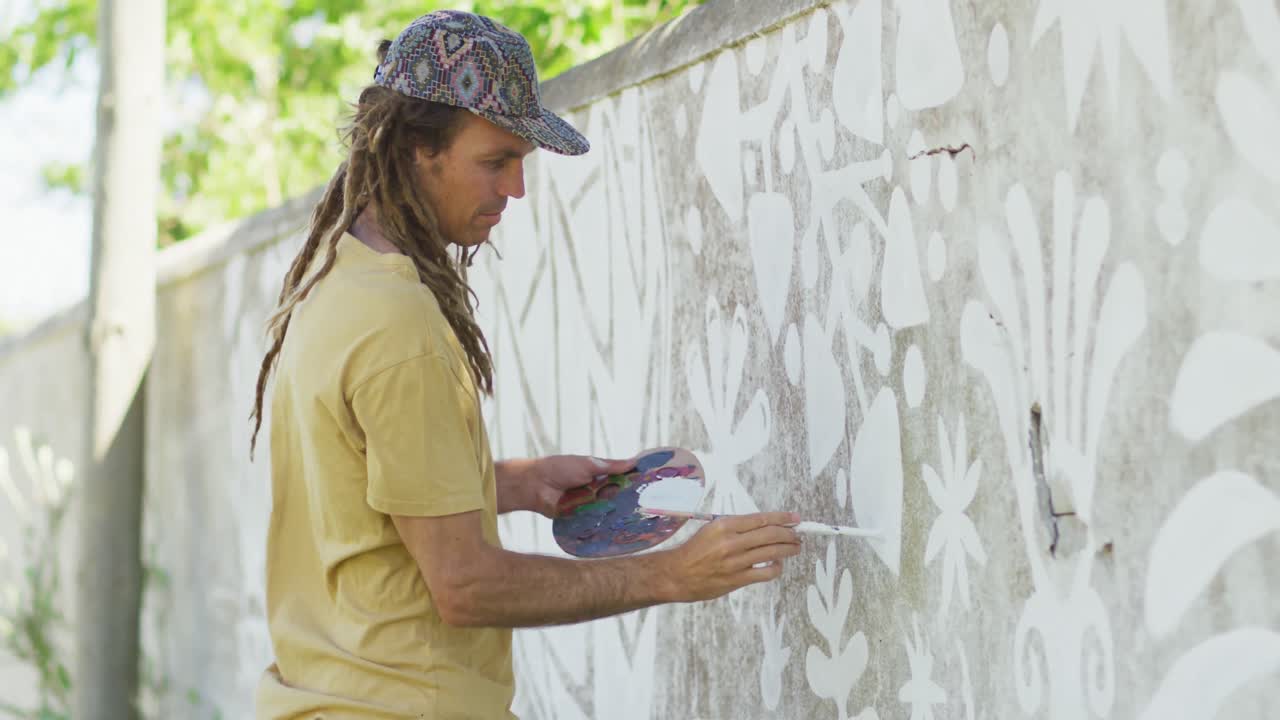 video de un artista masculino caucásico feliz con rastas pintando un mural en la pared