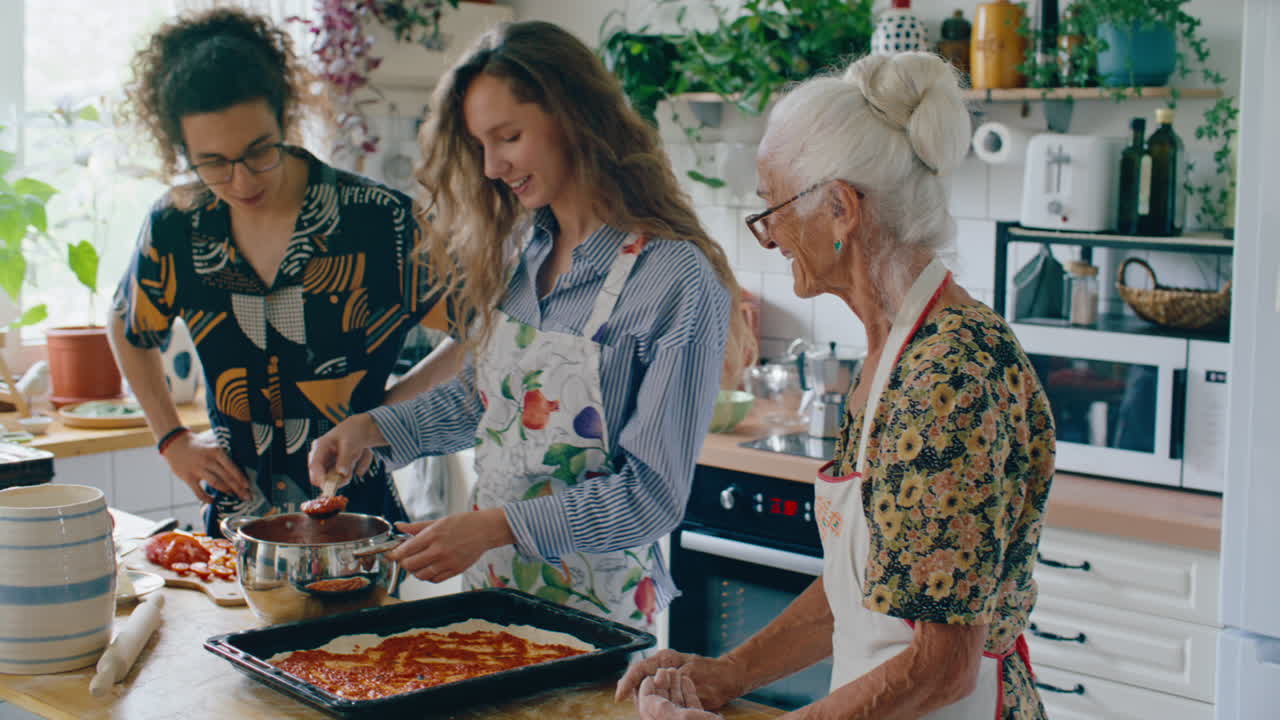 Frau verteilt Sauce auf Pizzateig beim Kochen mit der Familie in der Küche