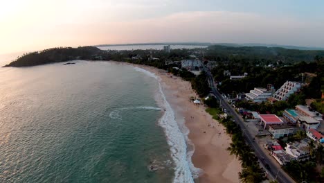 Muñeca-Aérea-Sobre-Personas-Que-Se-Relajan-En-El-Mar-Turquesa-Y-La-Arena-Cerca-De-Hoteles-Y-Bosques-En-La-Playa-De-Mirissa-Al-Atardecer,-Sri-Lanka