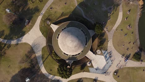 aerial top down showing round rooftop of famous planetarium in buenos aires - ascending shot with resting people outdoors in park